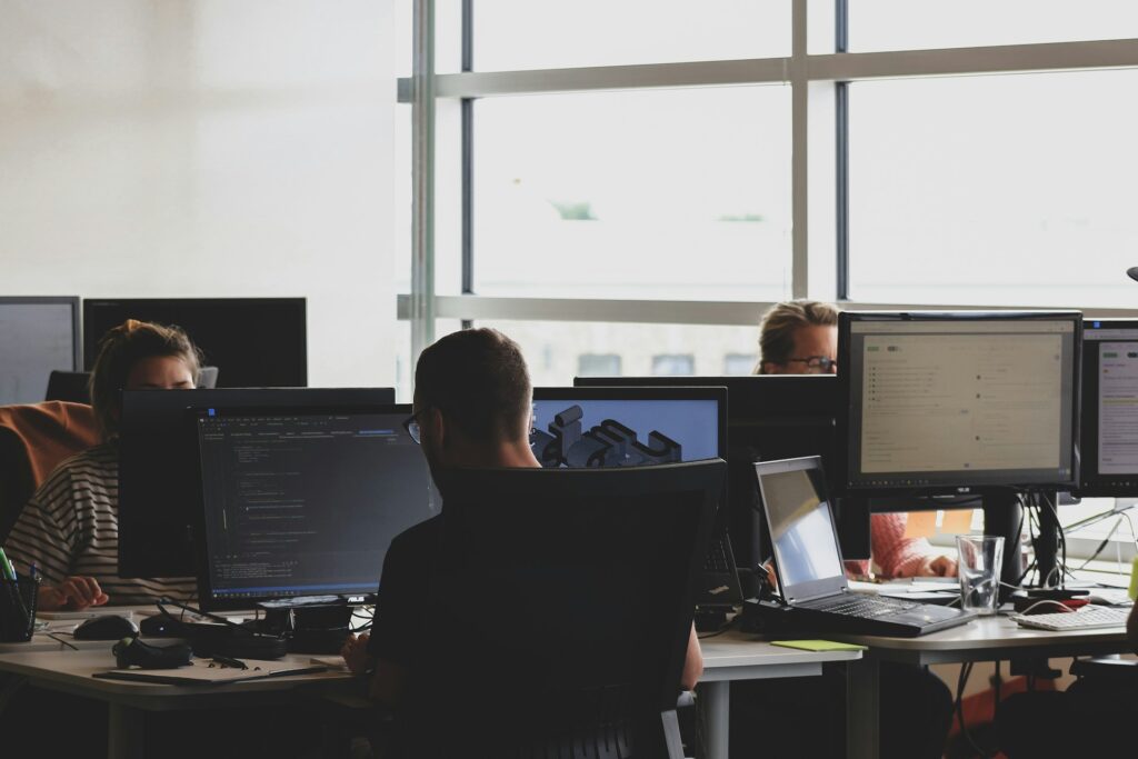 People working on computers in an office, with multiple screens displaying code and cybersecurity tools.