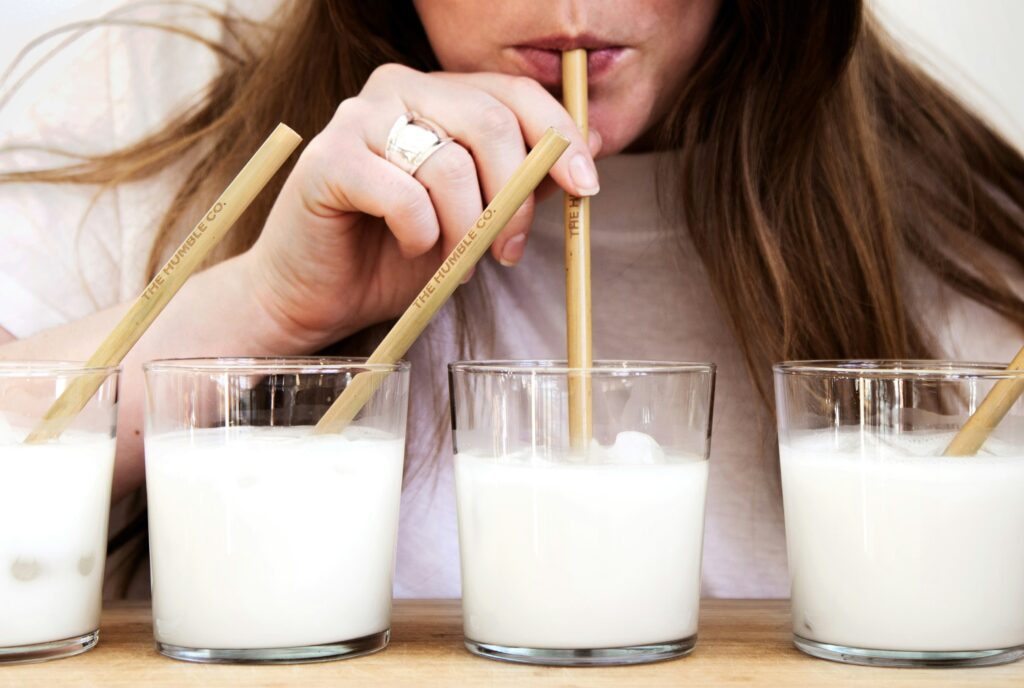 Person sipping fresh milk through a bamboo straw, highlighting the experience of drinking raw milk.