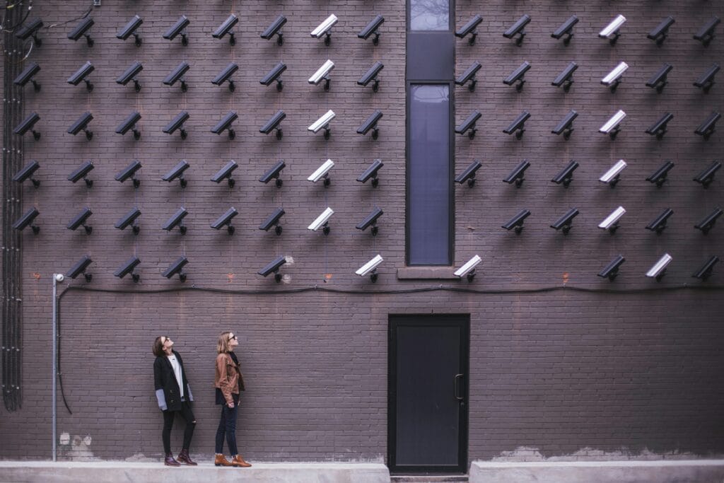 Women observing a wall covered with numerous security cameras in an urban setting, showcasing modern surveillance invading privacy