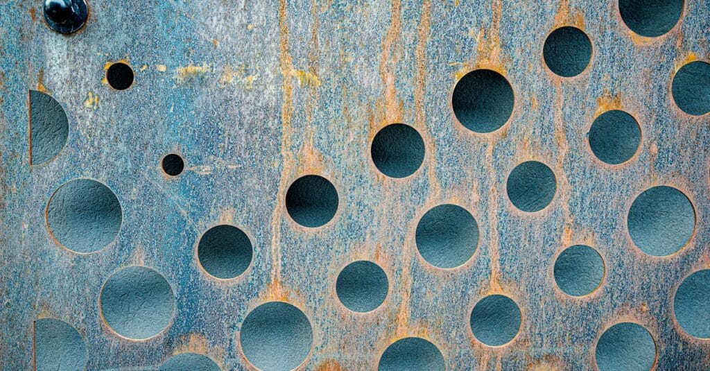 Close-up of a weathered rusty metal surface featuring circular holes, showcasing texture and grunge style to signify a port forward rule and port forwarding to access internal services 